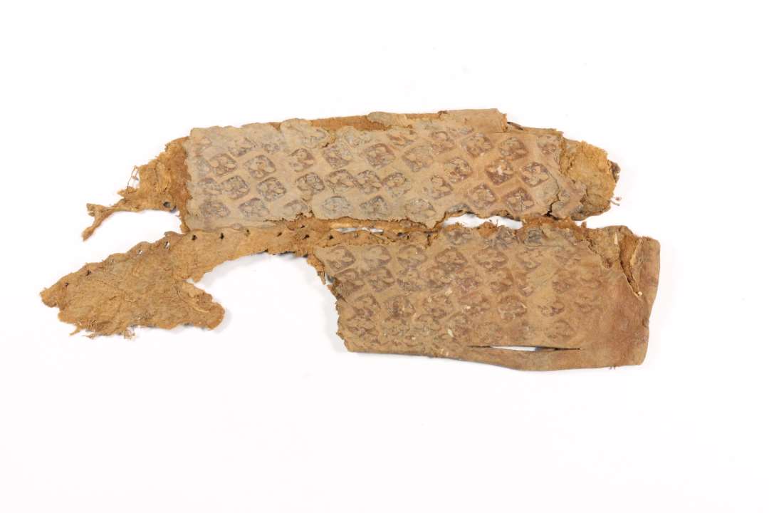 Fragment af knivskede af læder. Ornamenteret med indstemplede franske liljer. Længde: 11,5, bredde: 4,6 cm.