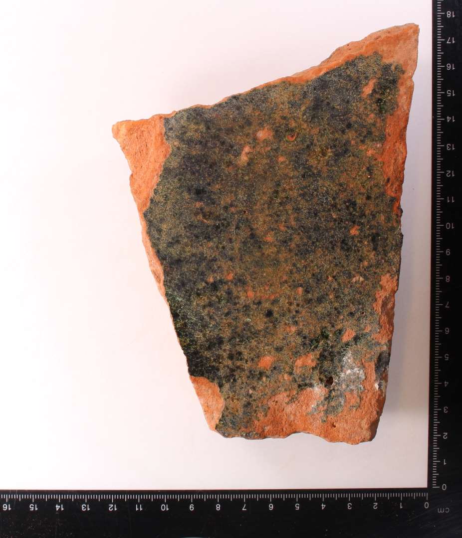 Fragment af kvadratisk gulvflise. Mørkegrøn glasur. Tykkelse: 2,8 cm.
