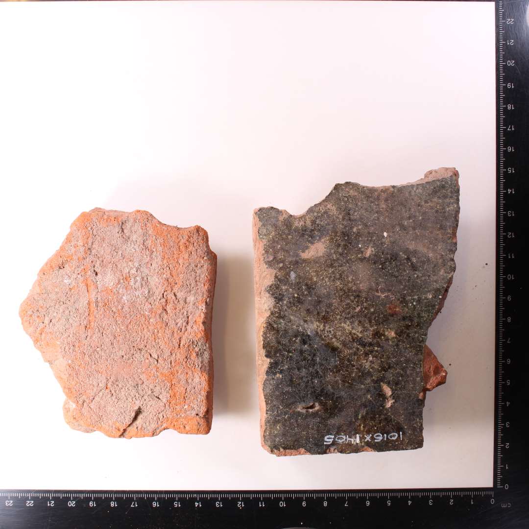 To fragmenter af gulvfliser. Den ene med mørkegrøn glasur, den anden uden rester af glasur. tykkelse: h.h.v. 2 og 2,5 cm.