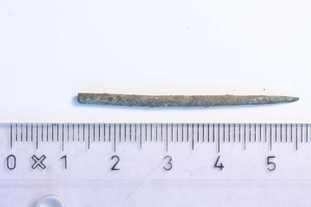 En nål af kobberlegering (4,2 cm). Nåleøjet erkendes ikke og formodes at må være knækket af.