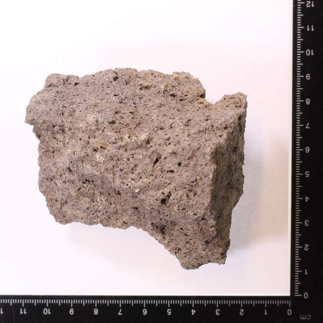 Frasgment af kværnsten af basalt. Kantstykke, med hugspor på én flade, samt kanten. Min. 6 cm tyk, men afbrudt. 