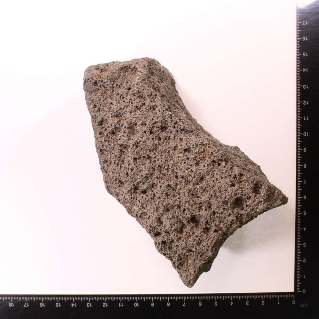 Fragment af kværnsten af basalt. Flot stykke, med del af midterhul der har ophævet vulst. Hugspor på siden med vulst. Slidspor på STENSUP[4]: modsatte side. 6,2 cm tyk.