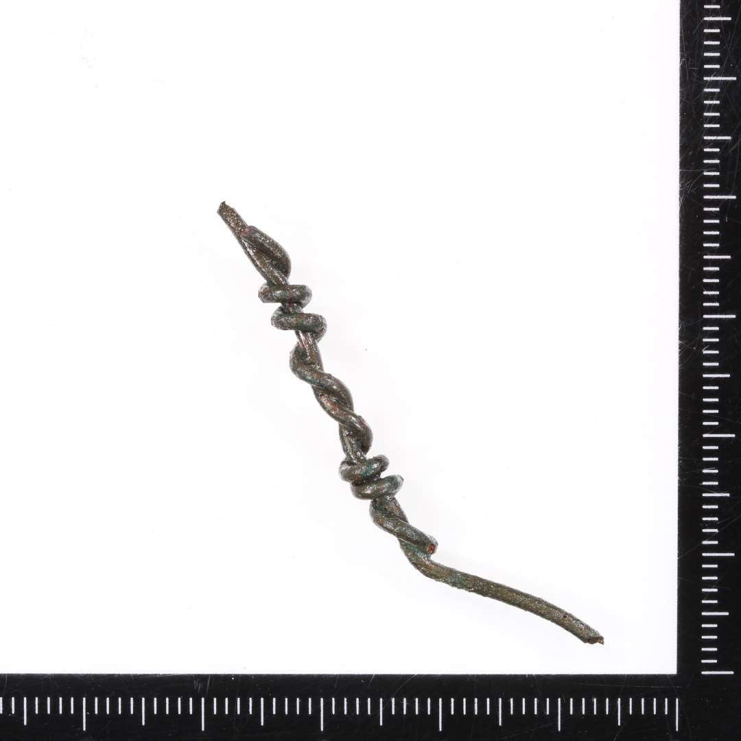  Bronzetråd. To tråde viklet om hinanden. Samlet længde ca. 4,8 cm, Tværsnit rundt, ø ca. 1 mm.