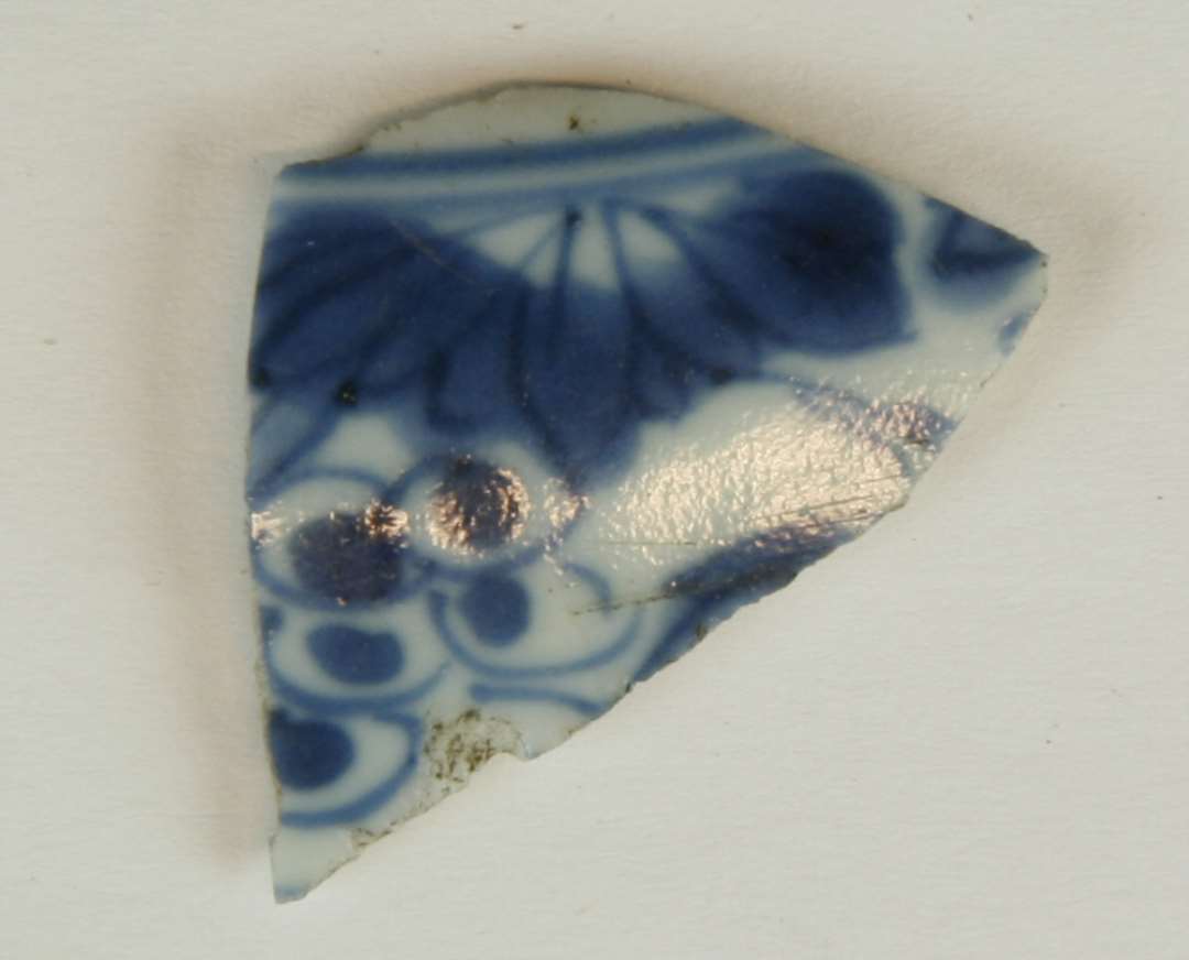 Sideskår fra tallerken af porcelæn med blåmalet blomstermotiv.