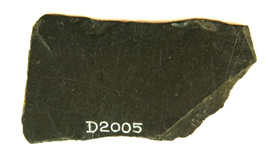 Fragment af skiferplade af uregelmæssig rektangulær form, ca. 4,4 x 7,7 cm.