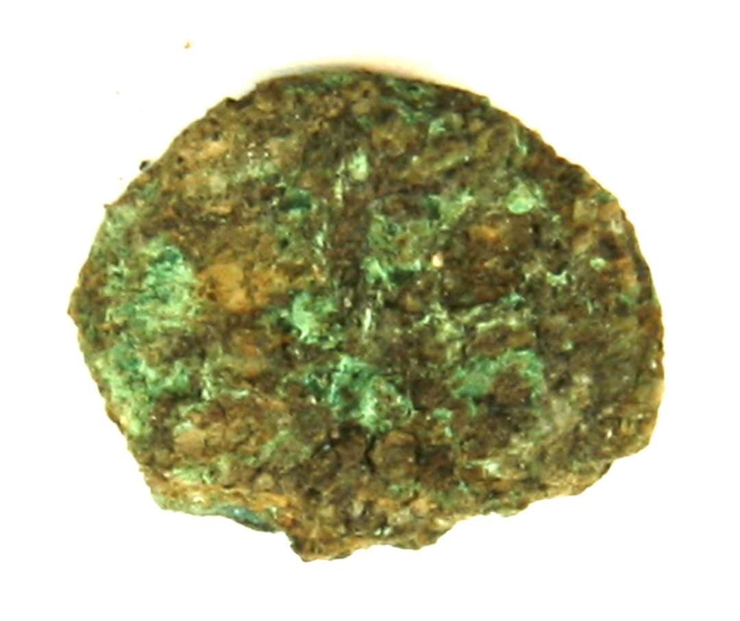 Kobbermønt (?) med kraftig irbelægning og fragmenteret i kanten. Største mål: cm. 1,5 x 1,8 cm.