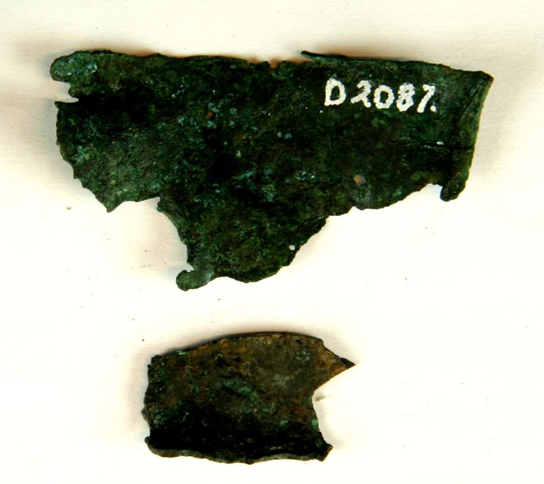 To stumper millimetertykt bronzeblik med afbrudte kanter og af let krummet, uregelmæssig form med kraftig irskorpe.  Største mål henholdsvis: 1,7 x 2,8 cm. og 3,1 x 5,7 cm.