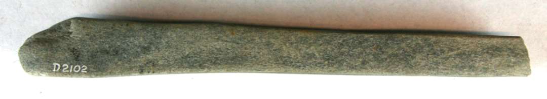 Stangformet hvæssesten af lysegrå sandsten med rektangulært tværsnit. Stenen er nedslidt på midterpartiet og udviser delvis afglattede brudar i begge ender, hvoraf den ene har klumpagtig form.Største længde: 22,3 cm. Bredde: 1,8 - 2,7 cm. Tykkelse: 1,5 - 2,4 cm.