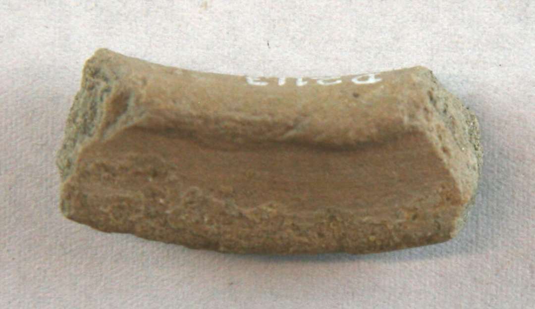1 skårstump, der udgør den øverste profilerede randkant af et mundingsrandskår af finslemmet grågulligt lergods med svage pletvise spor af klar blyglasur.