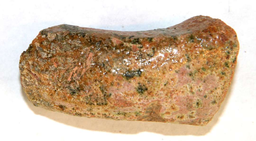 1 hankefragment af trind pølseform og af rødbrændt lergods, hvis yderside er dækket af ujævn klar og grønlig blyglasur.