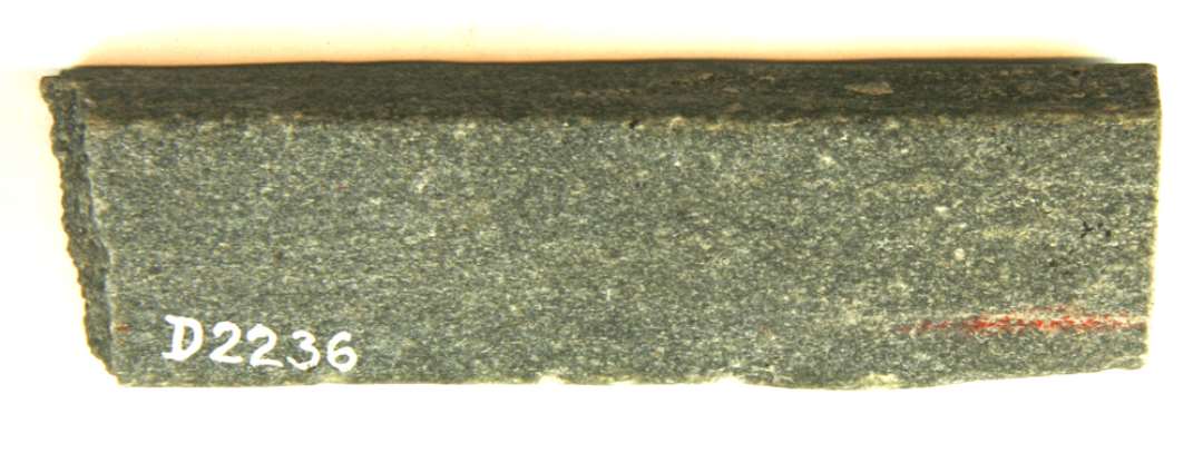 Fragment af flad stangformet hvæssesten af lysegrå sandsten af uregelmæssig rektangulær tværsnitsform og stærkt nedslidt langs den ene kant. Stenens ene ende fremtræder som et afrundet brud, medens den modsatte ende står i skarpt brud. Længde: 10,1 cm. Bredde: 2,6 cm. Største tykkelse: 1,3 cm.