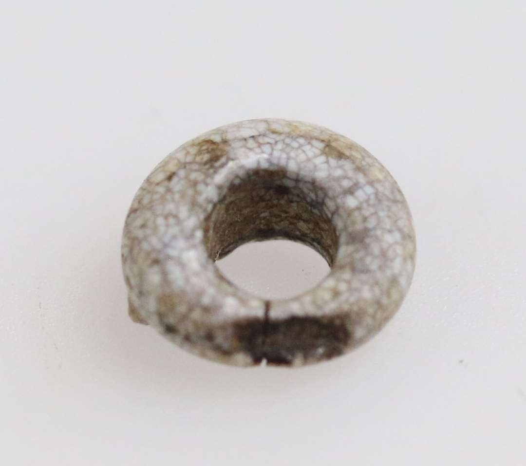 Meget lille perle af dekomponeret gråligt glas. Diameter: ca 0,5 cm.