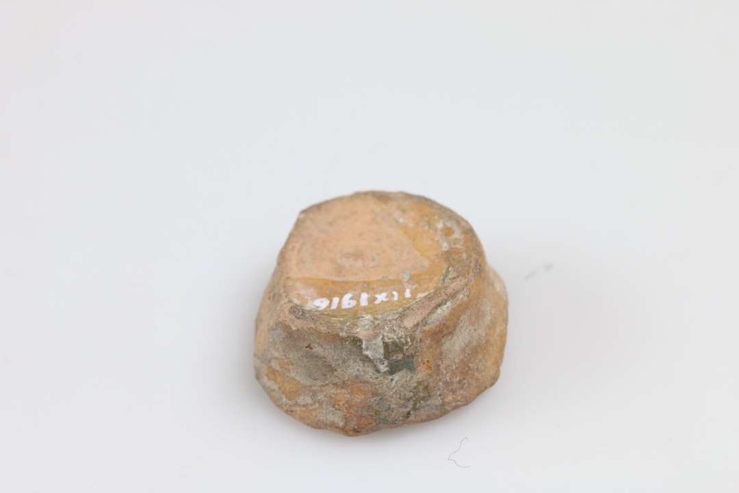 Skår af miniature lerkar/salvekrukke/rangle med flad bund, orange gods og klar glasur. Bunddiameter: 2,4 cm.