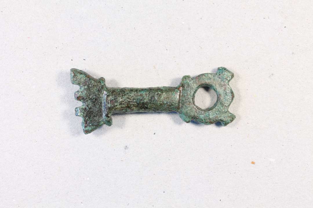 Støbt bronzenøgle, oprindelig med cirkulær fane, der nu er brækket. L. 4,2 cm. Modsat fanen et cirkulært hoved med hul igennem og to små 'ører'