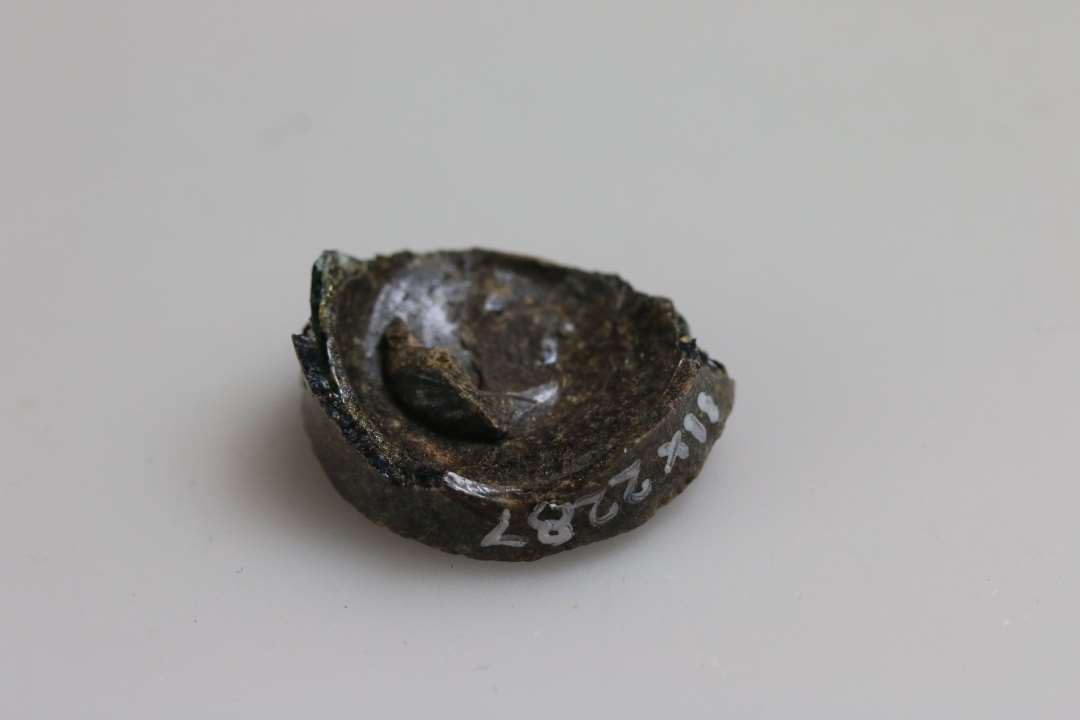 Bundskår fra meget lille beholder, et glas eller en 'salvekrukke', stammer fra midten af 1200-tallet. Ret nedbrudt. Diameter: ca 2,5 cm.
