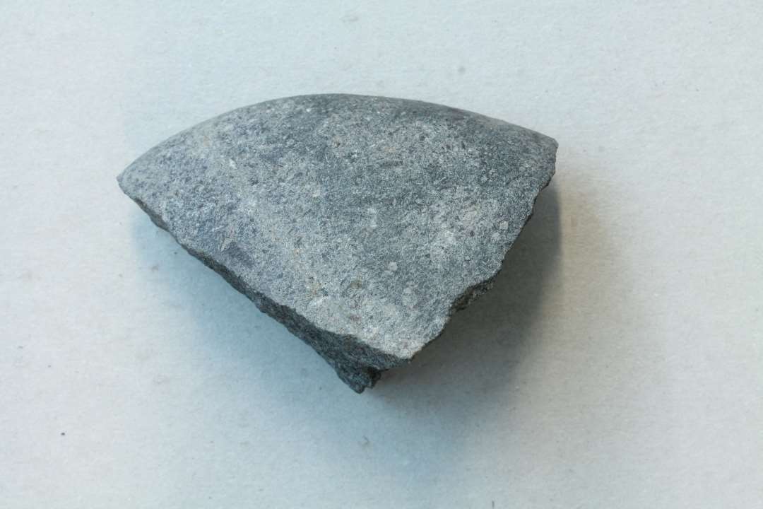 Fragment af oprindelig oval glat sten. Kan muligvis være fragment af sømglatter. Største mål: 6,3 cm.