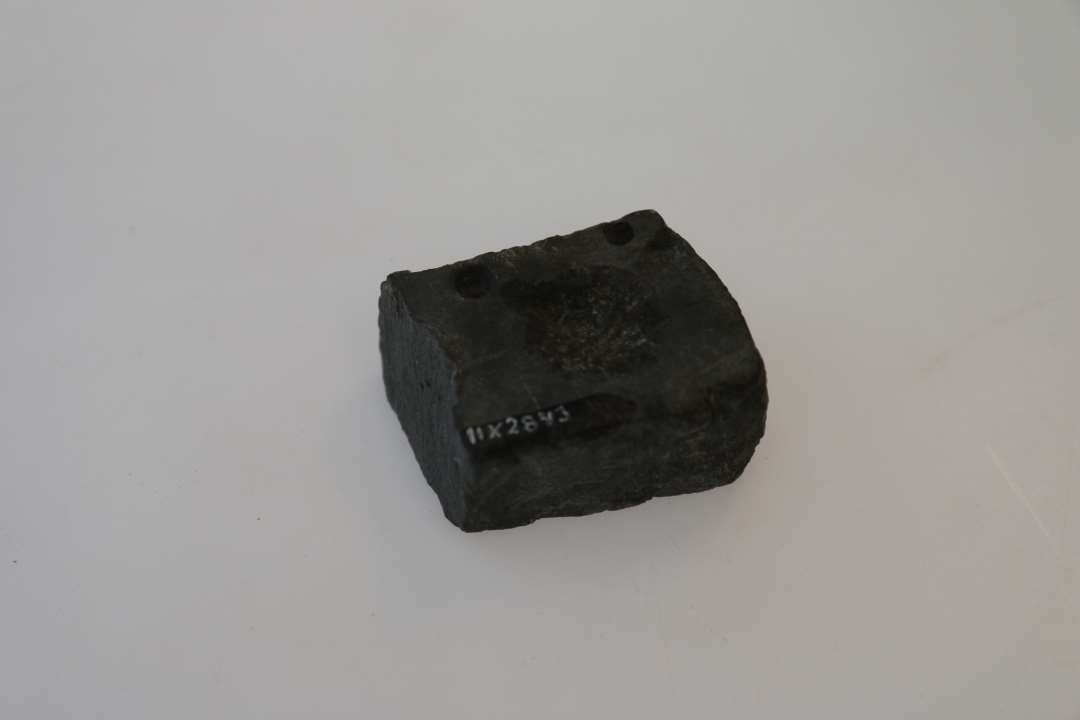 Fragment af støbeform i sten med to pashuller. Borthugget (centralt?) parti. På den anden side sliberidse, måske fra slibning af nåle. Mål: 5,2x4,3x2,9 cm. Mørk kalksten?