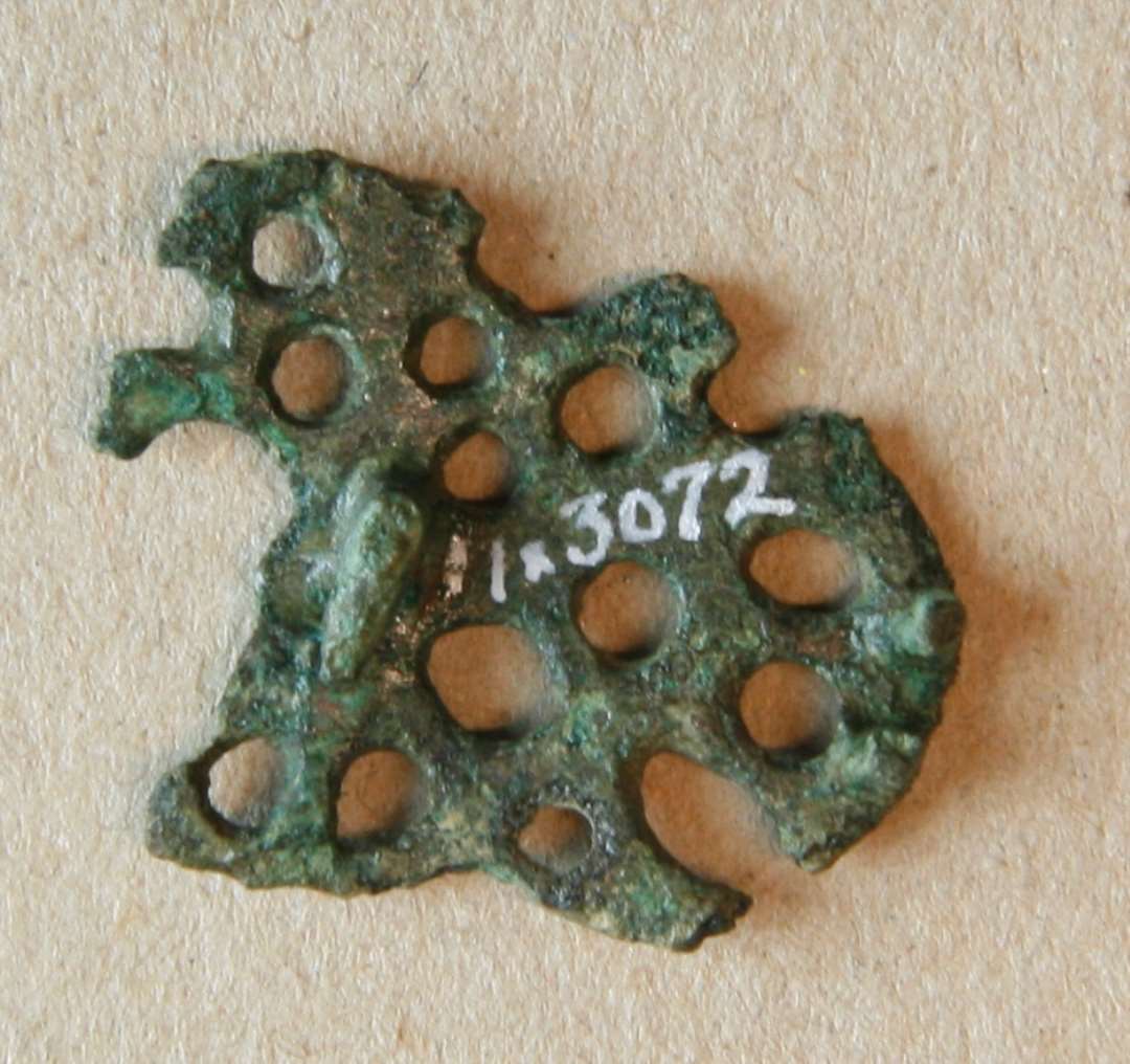 Større fragment af Urnesfibel, ca. 2 x 3 cm. Kons.  Identisk (samme form) med spændet ASR1021x23, Type m. tværstreger før tre små kløer