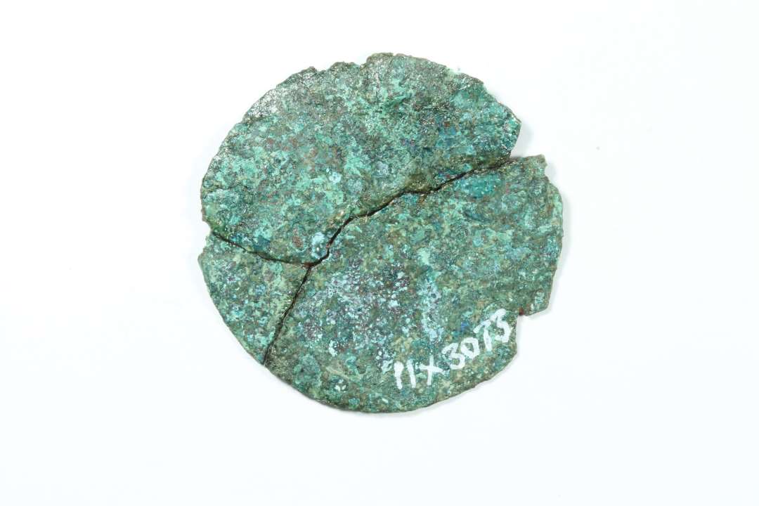 Cirkulært bronzebeslag i 3 fragmenter.  Ingen spor af ornamentik eller ophæng, men der kan have været en afbrækket øsken. Hængepynt? diameter: 3,4 cm.