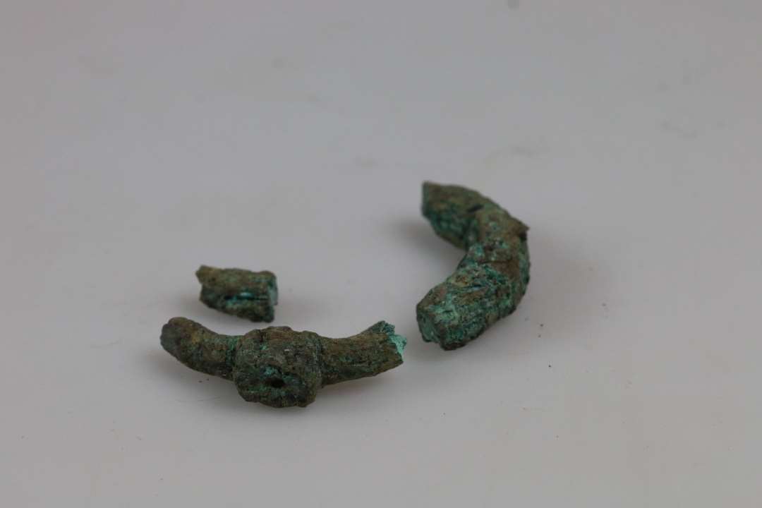  Fragmenter af bronzeringspænde Ø: (anslået) 4-5 cm. Nok for kraftigt til dragtspænde, måske bæltespænde? Ukonserveret
