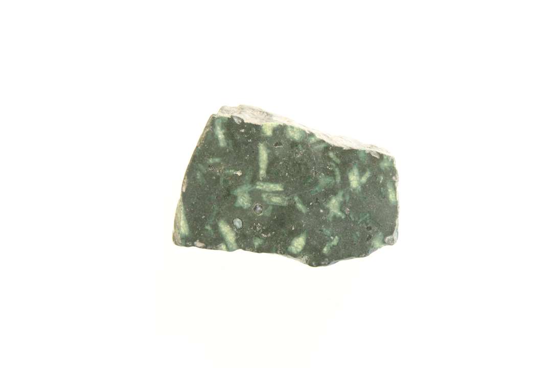 Fragment af poleret dækplade til helgengrav. Grønlig stenart, serpentin? Tykkelse 2 cm m. brud på alle fire sider.  Mål 6 x 4 x 2 cm.

Porfyr