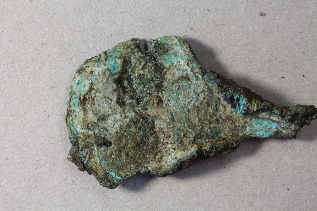 Negativt aftryk med rester af guldblik og bronze. Kons.  Korrosionsskal. Største mål: 4 cm.
