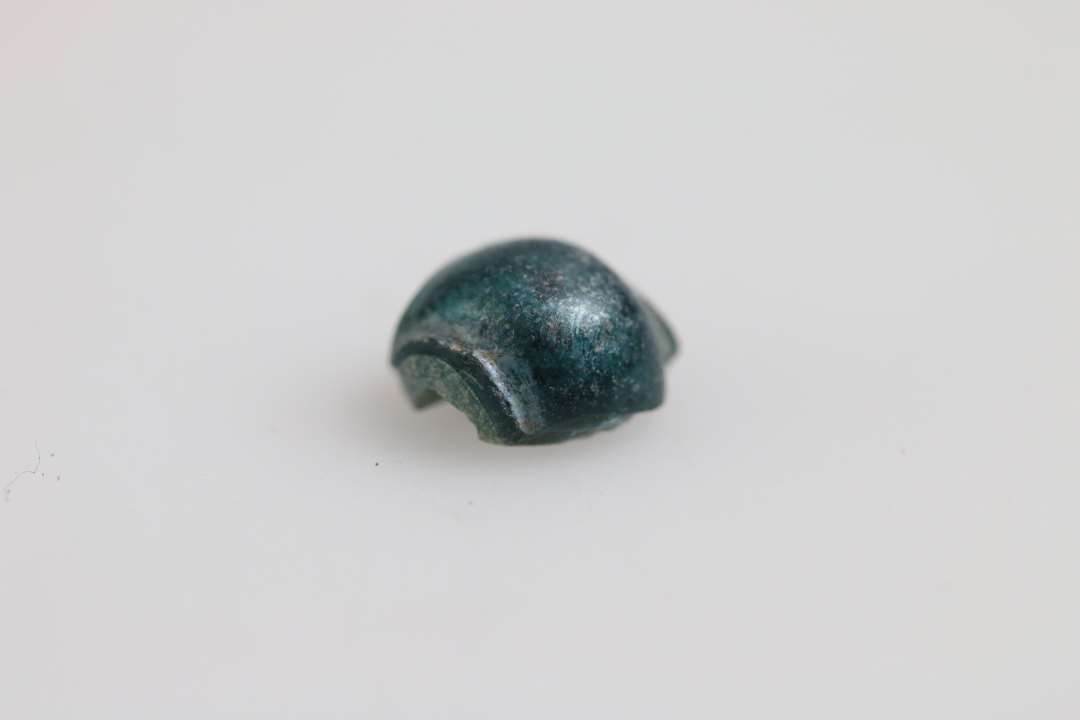 Perle, halv vistnok af uigennemsigtigt blåligt glas overtrukket med klart blåt glas. Et halvt segment. Største mål: ca 0,6 cm.