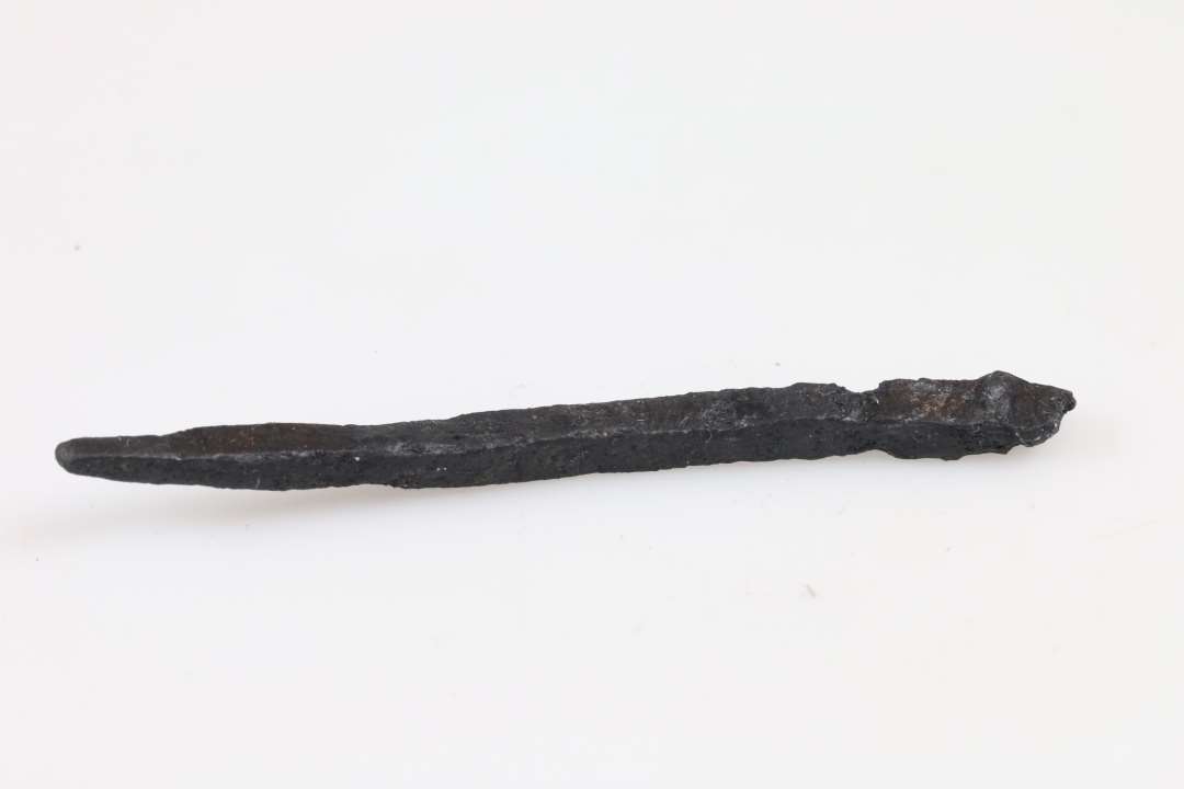 Fragment af aflang genstand, spids i den ene ende, firsidet tværsnit. Længde: 8 cm., Konserveret