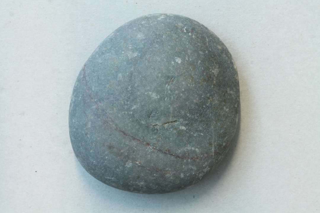 Flad, let oval utaldannet natursten af en meget tæt stenart med meget glat overflade. Kan meget vel have været anvendt som sømglatter. Største diameter: 8,5 cm.