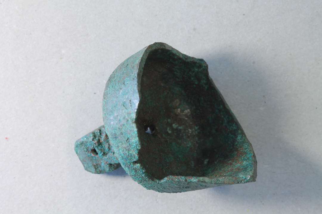 Bronzeklokke. Kons.  Fragment af lille støbt klokke, hvor randen af brækket af, ø. ca 4 cm.

Håndklokke