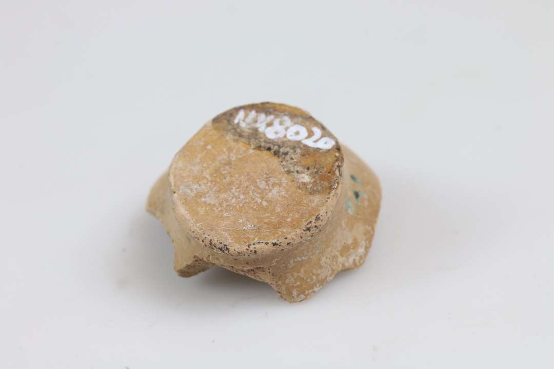 Skår af fladbundet miniature lerkar/salvekrukke/rangle, lysorange gods og klar glasur. Bunddiameter: 2,5 cm.