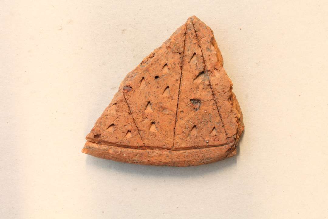 Fragment af låg med stregornamentik og indstemplede trekanter.  Største mål ca. 8 cm.