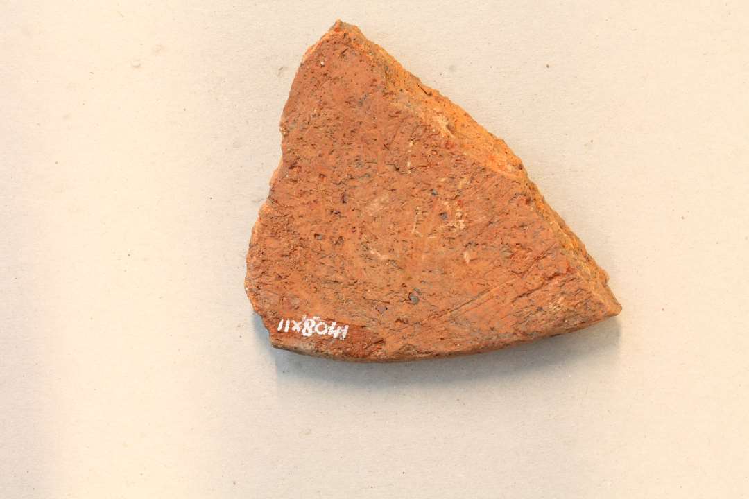 Fragment af låg med stregornamentik og indstemplede trekanter.  Største mål ca. 8 cm.