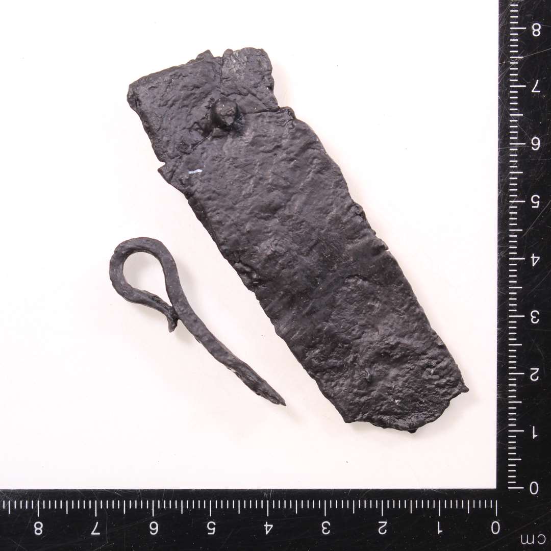 Et stykke båndformet jern med ombuk (mini gangjern), samt rektangulær jernplade med nitterest, beslag? Mål h.h.v.: 4,2 og 8 cm.