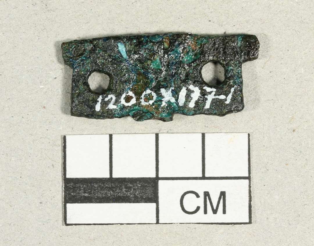 Fragment af beslag. Med to nittehuller. Mål: 2,2x0,9 cm.