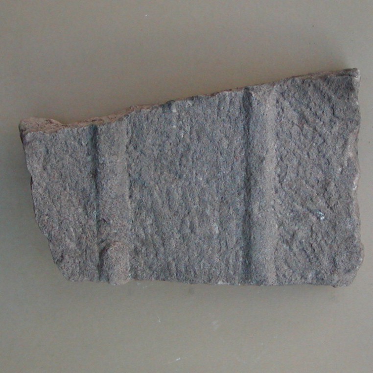 Fragment af låg til sandstenskiste. Med hugspor og to parallelle, ophøjede lister. Mål 33x21x8 cm.