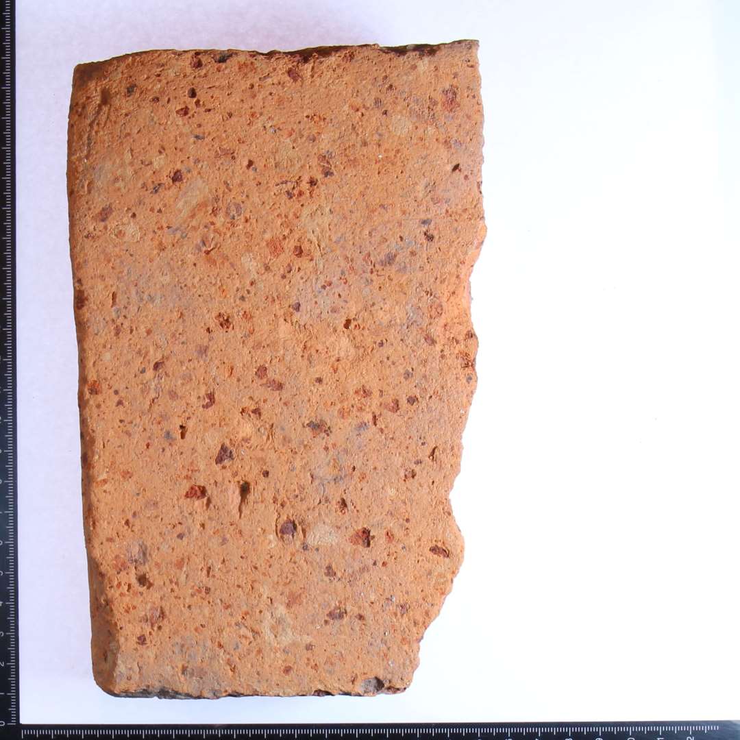 3/5 af slidt, rødbrændt gulvflise. Sidelængde 19 cm, tykkelse 4,5 cm.