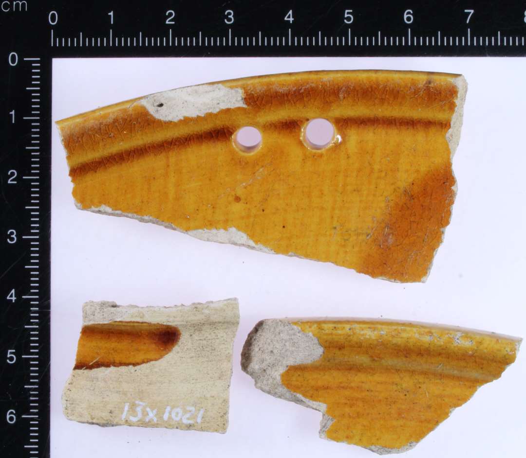 Tre sammenhængende randskår fra fad i lyst gult  gods med brungul dækkende glasur på inderside. To huller ved rand.