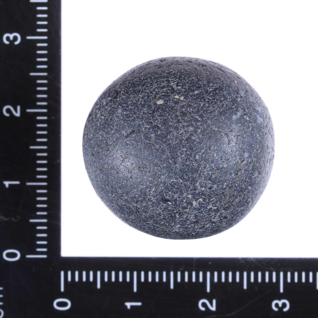 Lille kuglerund sort sten. Ca. 2 cm i diameter. Glatte overflader, som virker til at have slid.