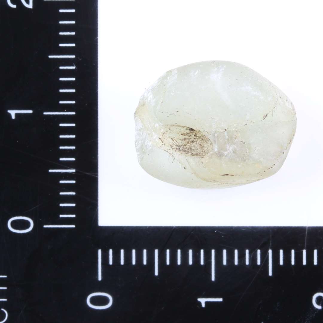 Ca. 1,5 x 1 cm hvid krystal. Fladslebet på den ene side, rå på de andre. Ca. 2 mm hul boret igennem.