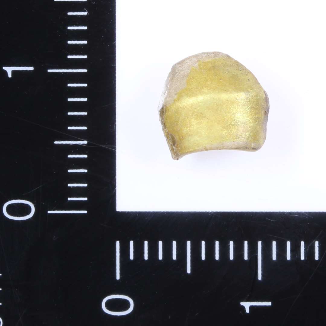 Fragment af dobbeltkonisk guldfolieret glasperle. Ca. 0,7 cm i længden og 0,6 cm i diameter.
