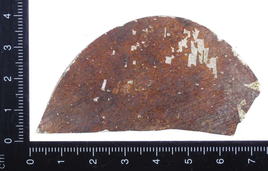 Fragment af vinduesglas med rundet klippet kant. 7,5 x 4 cm. Rødbrun bemaling på den ene side. Ruden i sin helhed kan have haft oval eller halv-oval form.