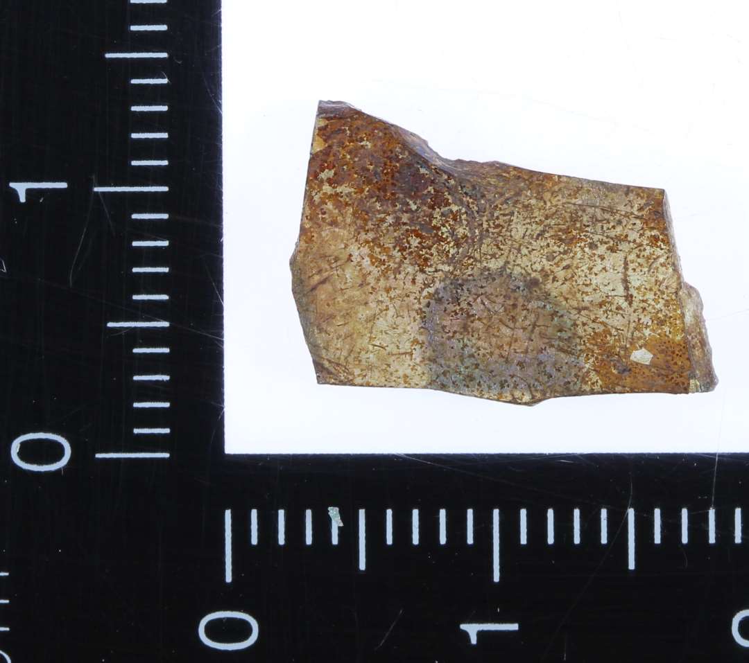 Lille fragment af brunfarvet og dårlig bevaret glas.