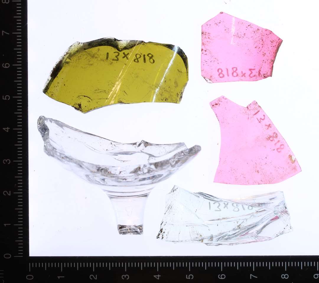 Bund af vinglas med rest afstilk i klart glas, fragment af 1,2 cm tykt fladt klart glas, fragment af buet grønbrunt flaskeglas og to fragmenter af tyndt buet rosa glas.