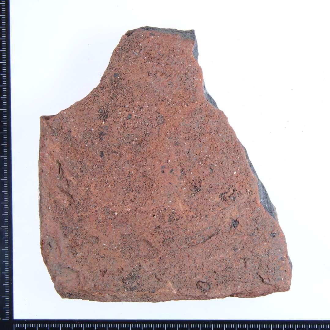 Et hjørne fragment af rødbrændt gulvflise. Største mål: ca. 9x7x3 cm. 
