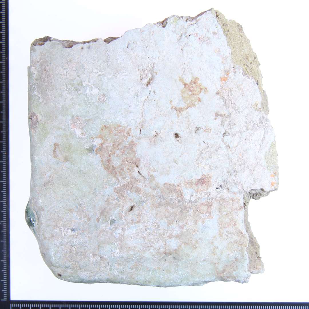 Et fragment af en gulvflise gulligbrændt med lysgrønlig glasur. Største mål: ca 10x9x6 cm.