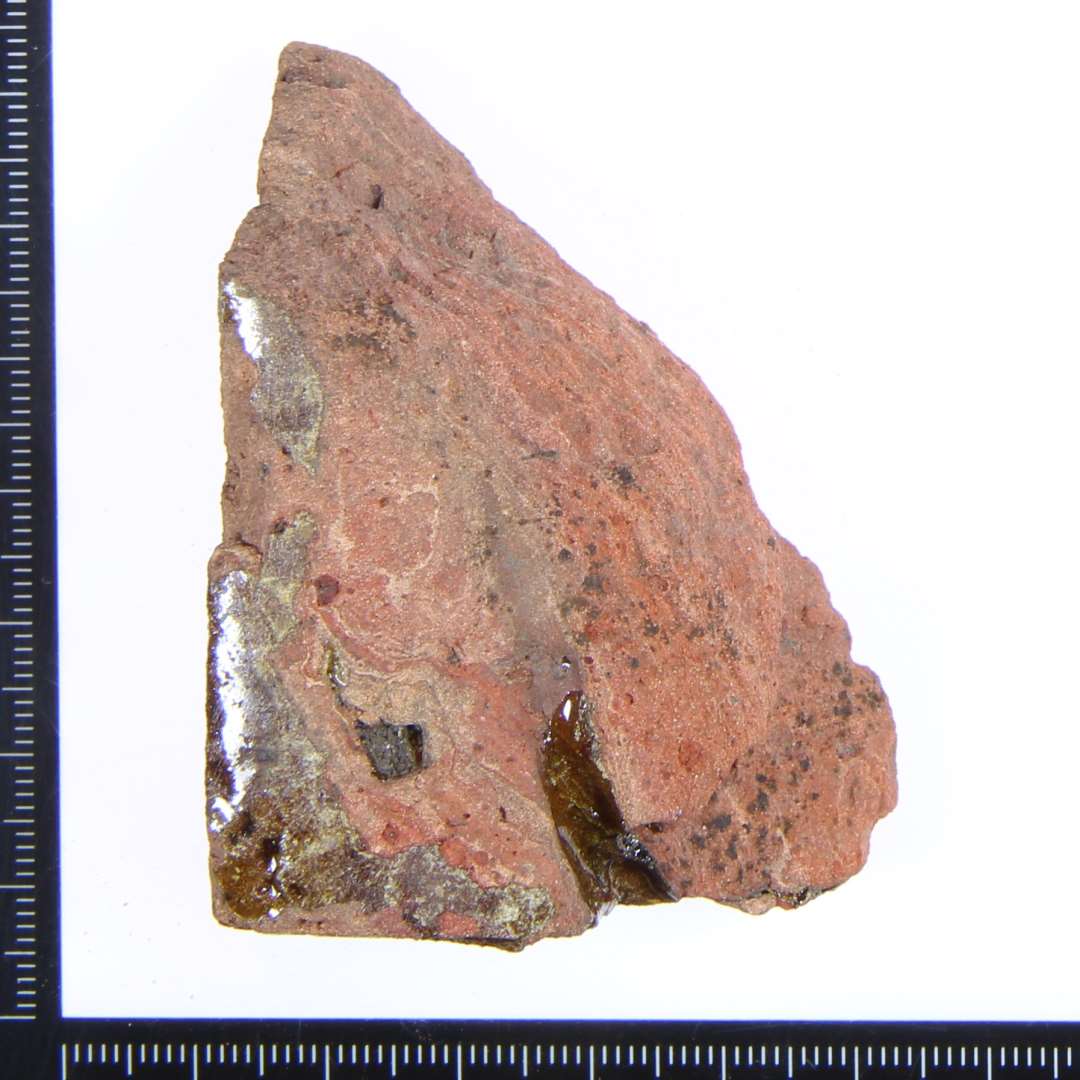 Et lille rødbrændt hjørne fragment med rester af rød/gul/grønlig glasur. Største mål: 5x4,5x ca.3 cm.