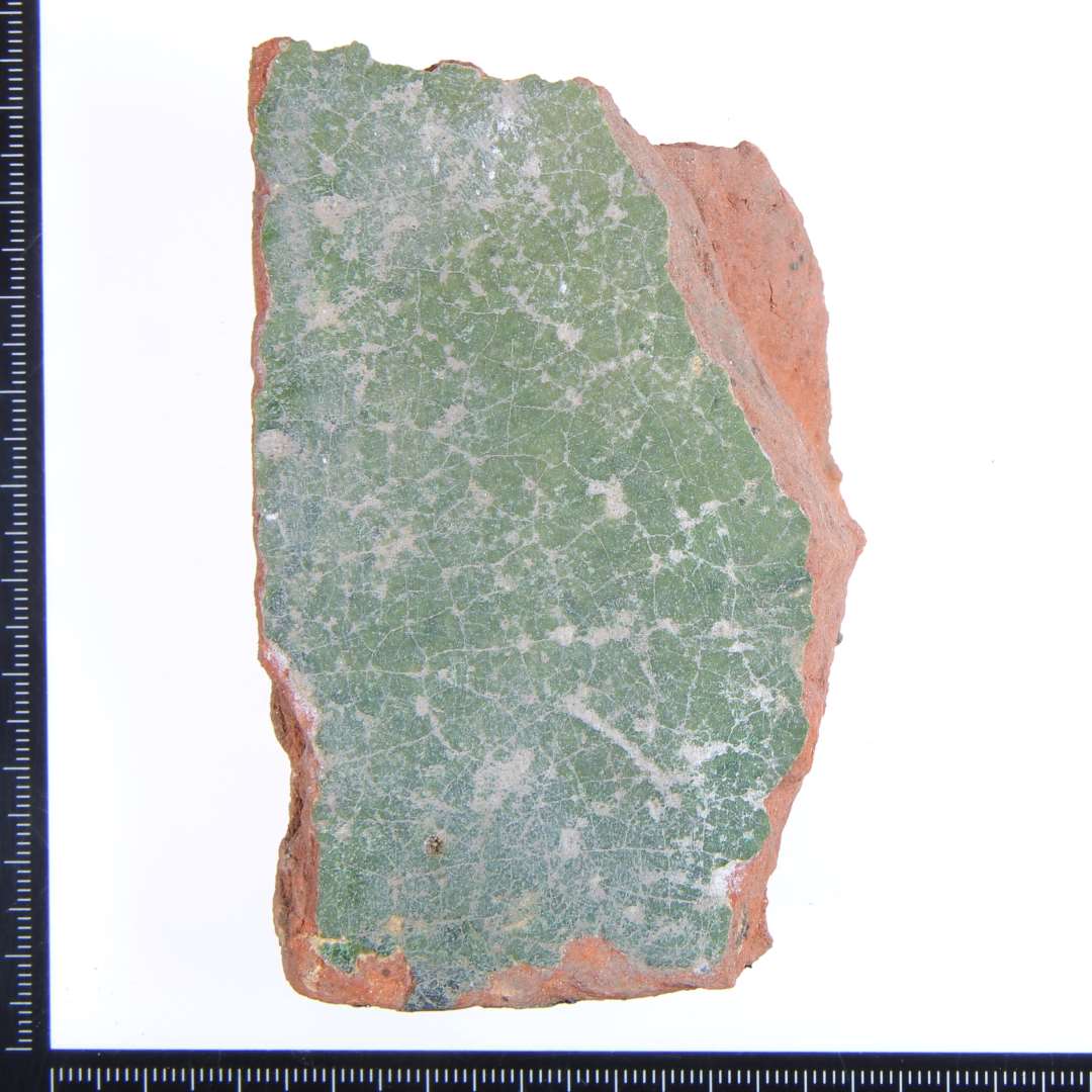 Et rødbrændt hjørne fragment med grøn glasur på oversiden. Største mål: 9x4,5x2,5 cm.