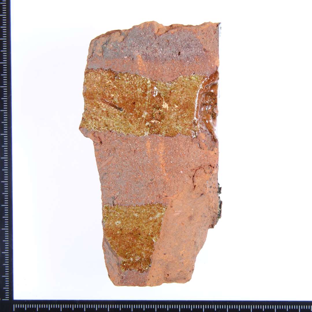 Et rødbrændt fragment med rester af rød og grønlig glasur. Størst mål: 10x5x3 cm.
