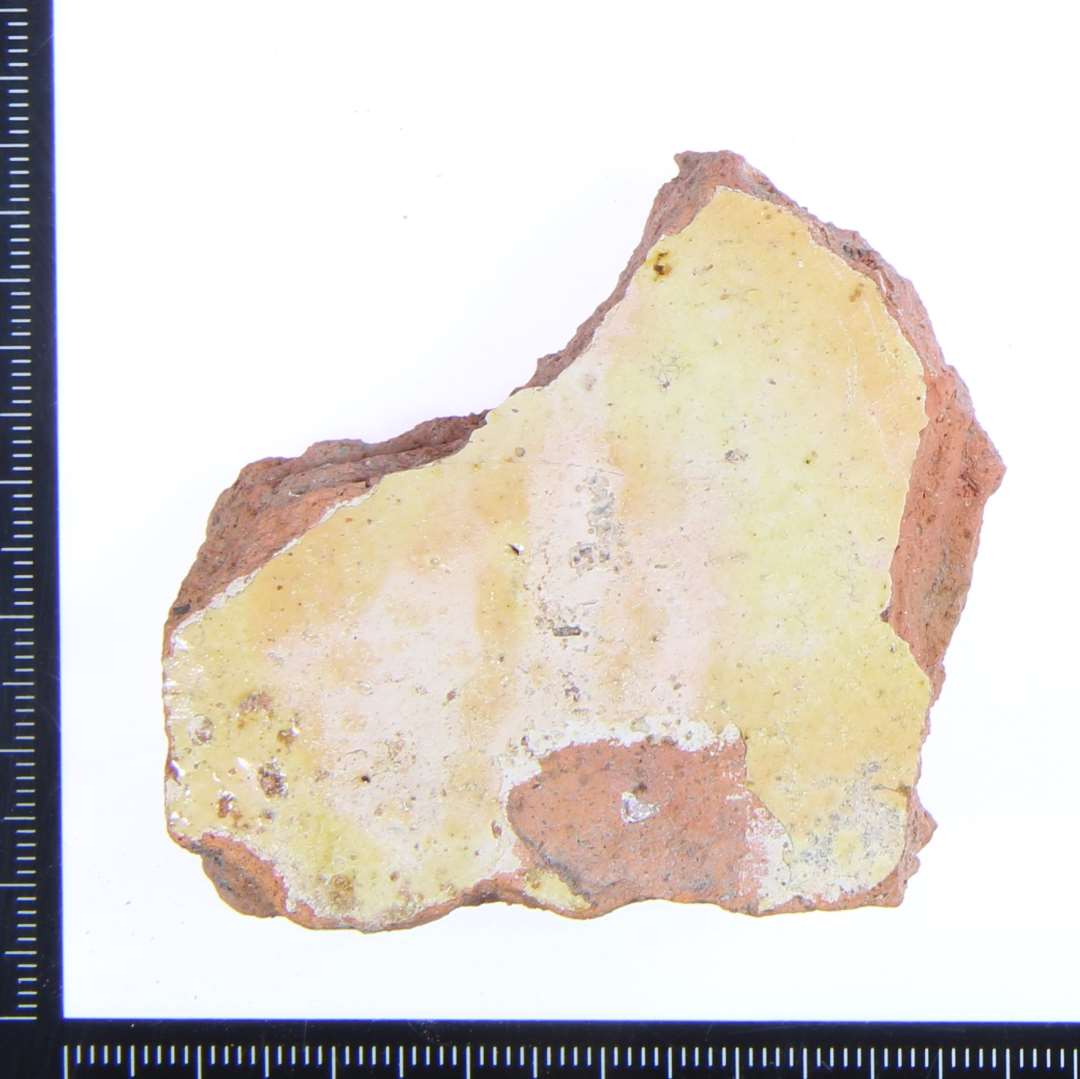 Et lille hjørne fragment med gullig glasur. Største mål: ca.5,5xx5x2 cm. 